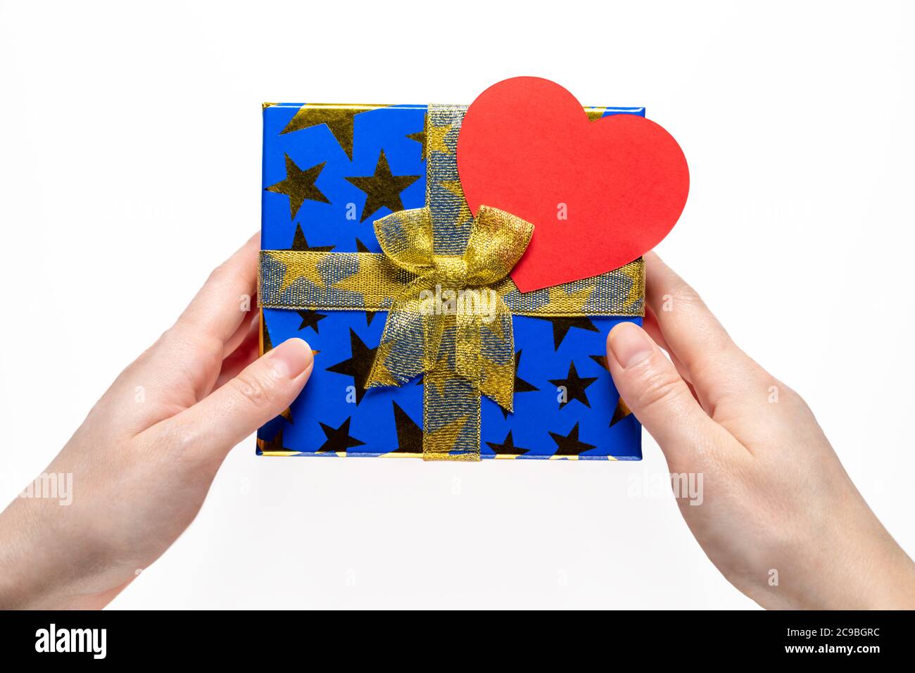 Gift or present box with golden ribbon and paper heart on white background with female hands top view. Stock Photo