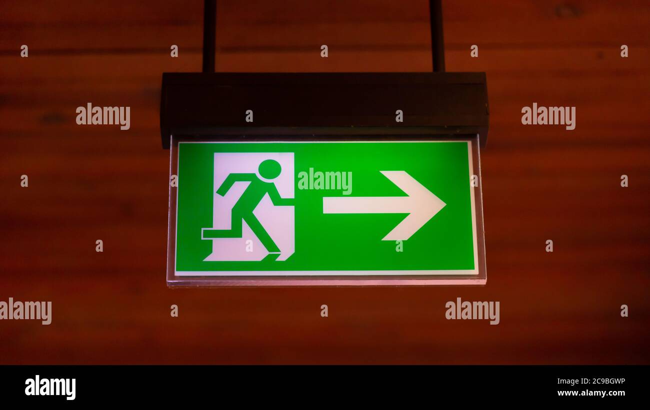Panorama with an illuminated emergency exit sign. Neutral, brown background. Stock Photo