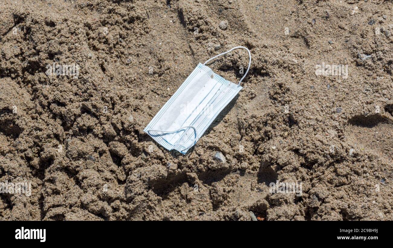 Travemünde, Schleswig-Holstein / Germany - June 24, 2020: Close up of a disposable surgical mask on a sand beach. Part of the 'New Normal' Stock Photo