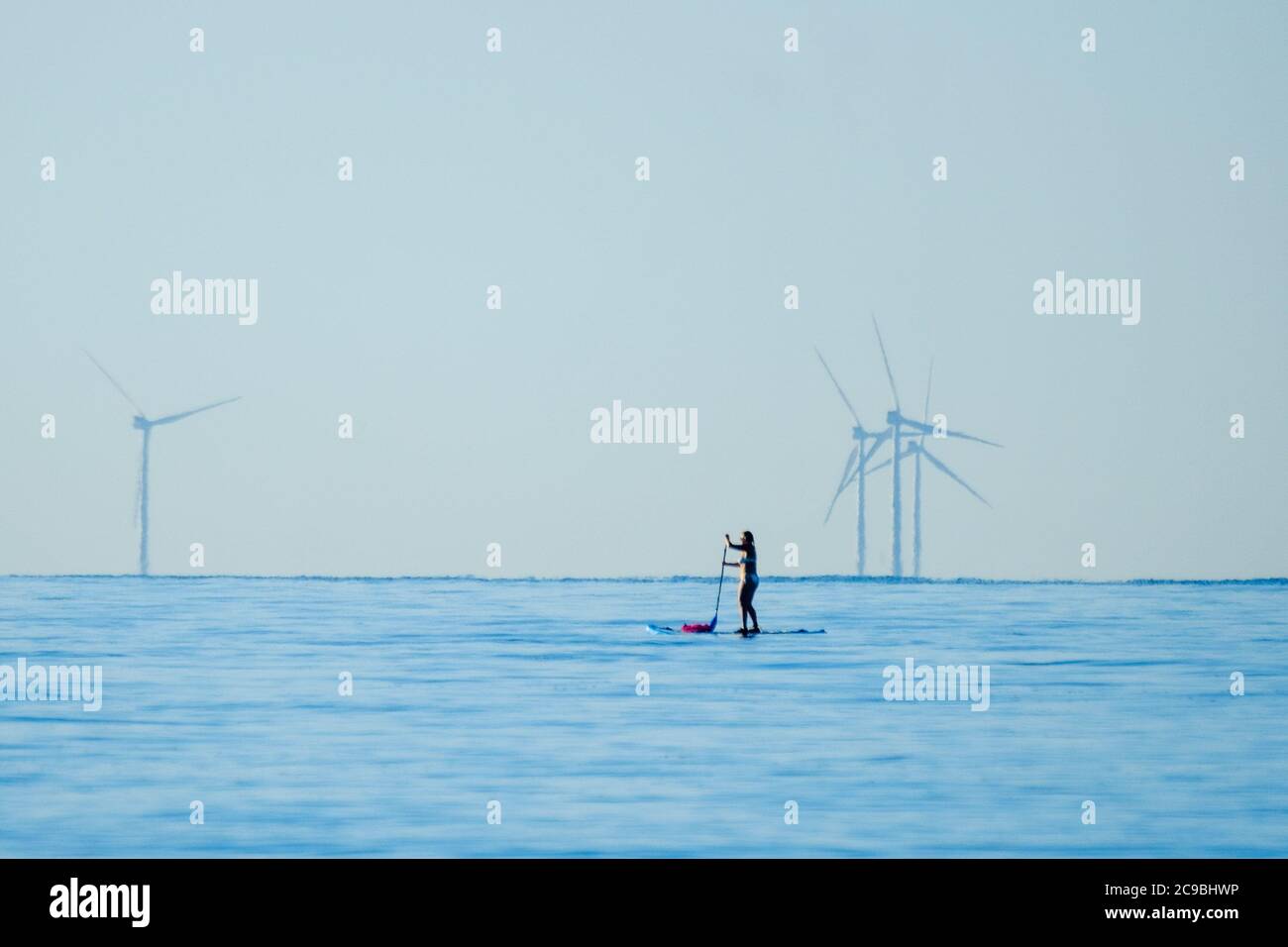 Worthing Beach, Worthing, UK. 30th July, 2020. Paddleboarders enjoy the calm morning sea . With a clear blue sky and flat waters people on paddle boards enjoy the early morning off the Sussex coast. Rampion Wind Farm can be seen 13-20km offshore. Picture by Credit: Julie Edwards/Alamy Live News Stock Photo
