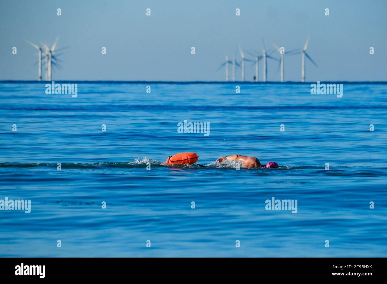 Worthing Beach, Worthing, UK. 30th July, 2020. Open water swimmers enjoy the calm morning sea . With a clear blue sky and flat waters people on paddle boards enjoy the early morning off the sussex coast. Rampion Wind Farm can be seen 13-20km offshore. Picture by Credit: Julie Edwards/Alamy Live News Stock Photo