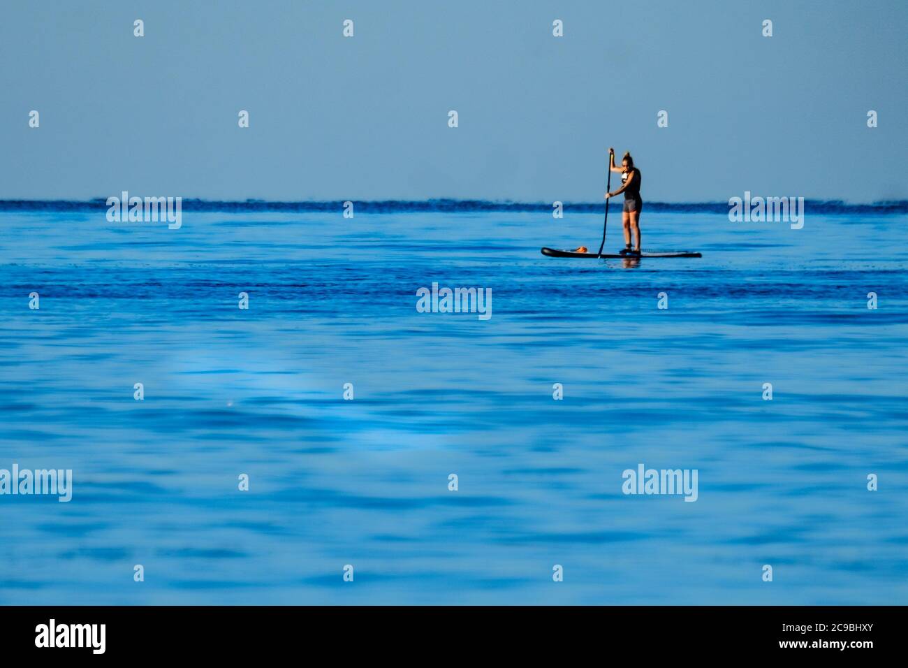 Worthing Beach, Worthing, UK. 30th July, 2020. Paddleboarders enjoy the calm morning sea . With a clear blue sky and flat waters people on paddle boards enjoy the early morning off the sussex coast. Rampion Wind Farm can be seen 13-20km offshore. Picture by Credit: Julie Edwards/Alamy Live News Stock Photo