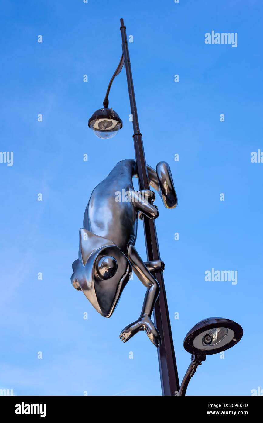 Giant stainless steel chameleon hanging from a lamp post, isolated on a deep blue sky. Stock Photo