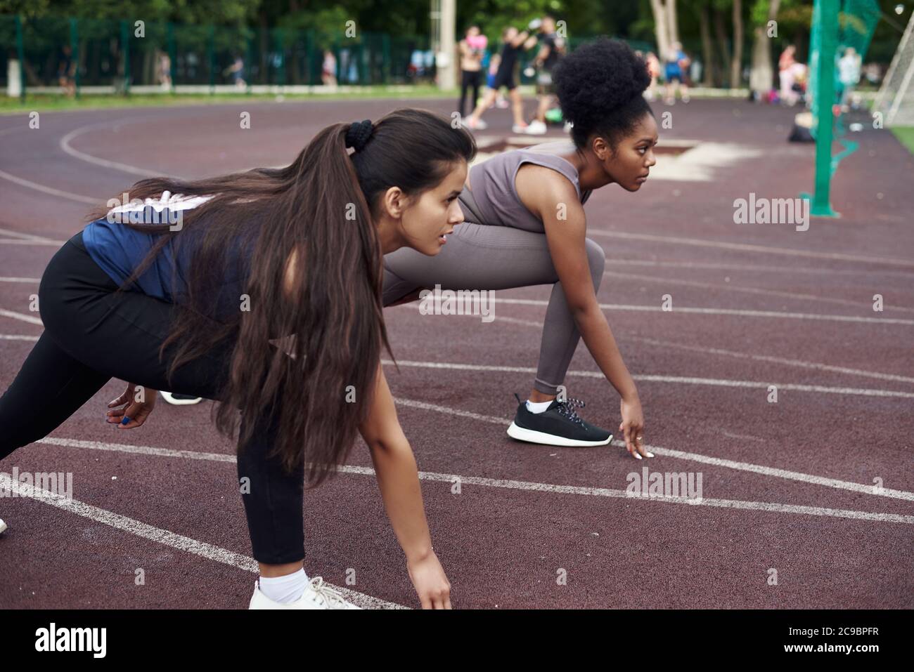 Rivals are ready to run outdoors. Reade set Go. A dark-skinned and a Caucasian girl stand in a start pose before running. Competition between two friends. Stock Photo