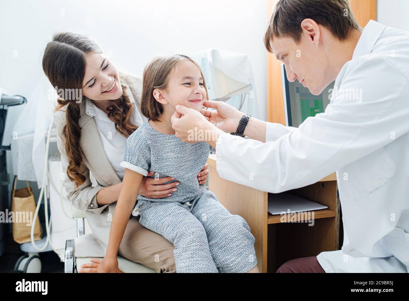 Social little girl in being examined by pediatrician, sitting on mom's lap Stock Photo