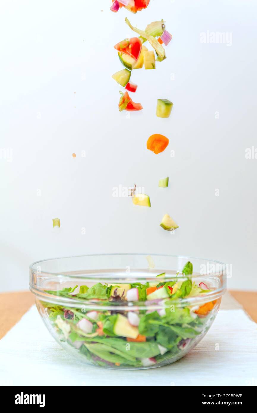 Pieces of fresh vegetables falling down into glass bowl creating