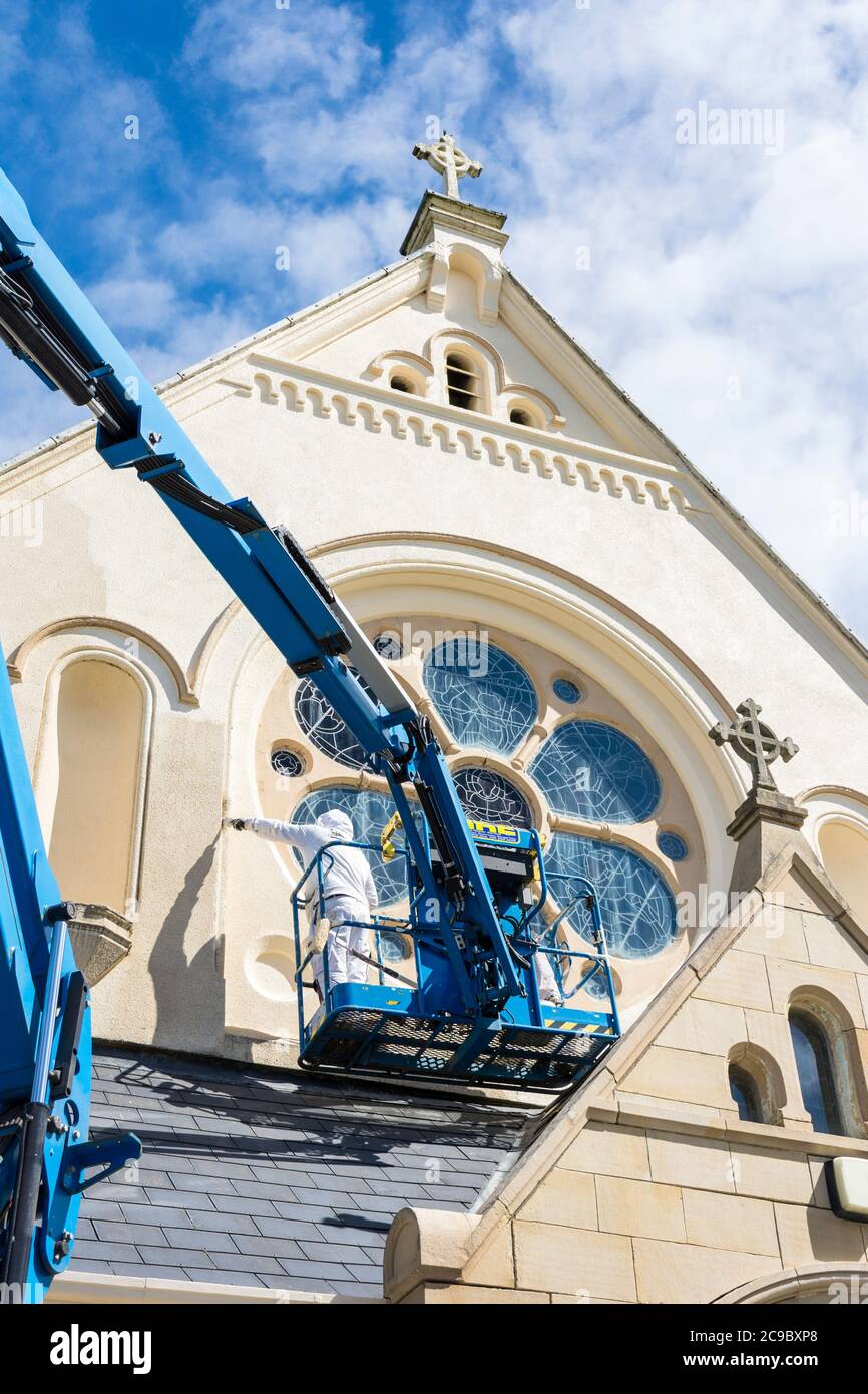 Men painting the exterior of Catholic Church. Covid 19 virus has reduced the church's income by 80% putting pressure on essential maintenance. Stock Photo