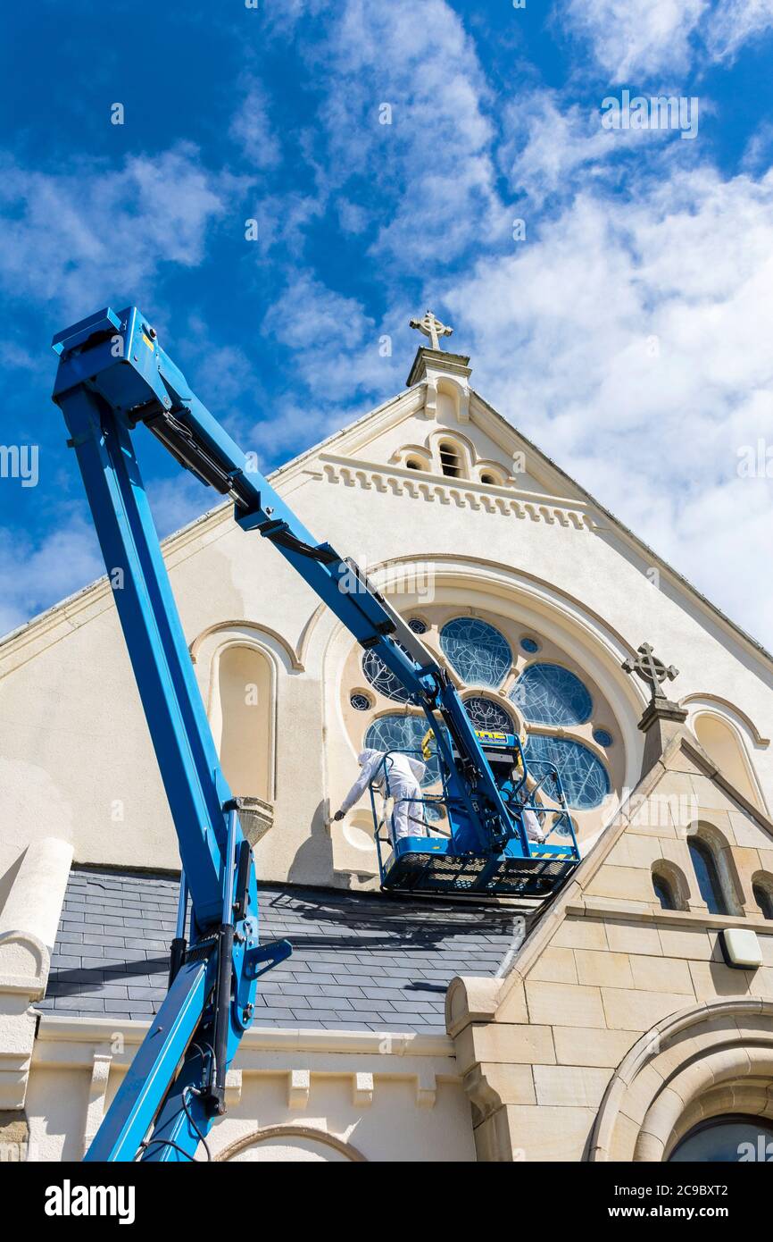 Men painting the exterior of Catholic Church. Covid 19 virus has reduced the church's income by 80% putting pressure on essential maintenance. Stock Photo