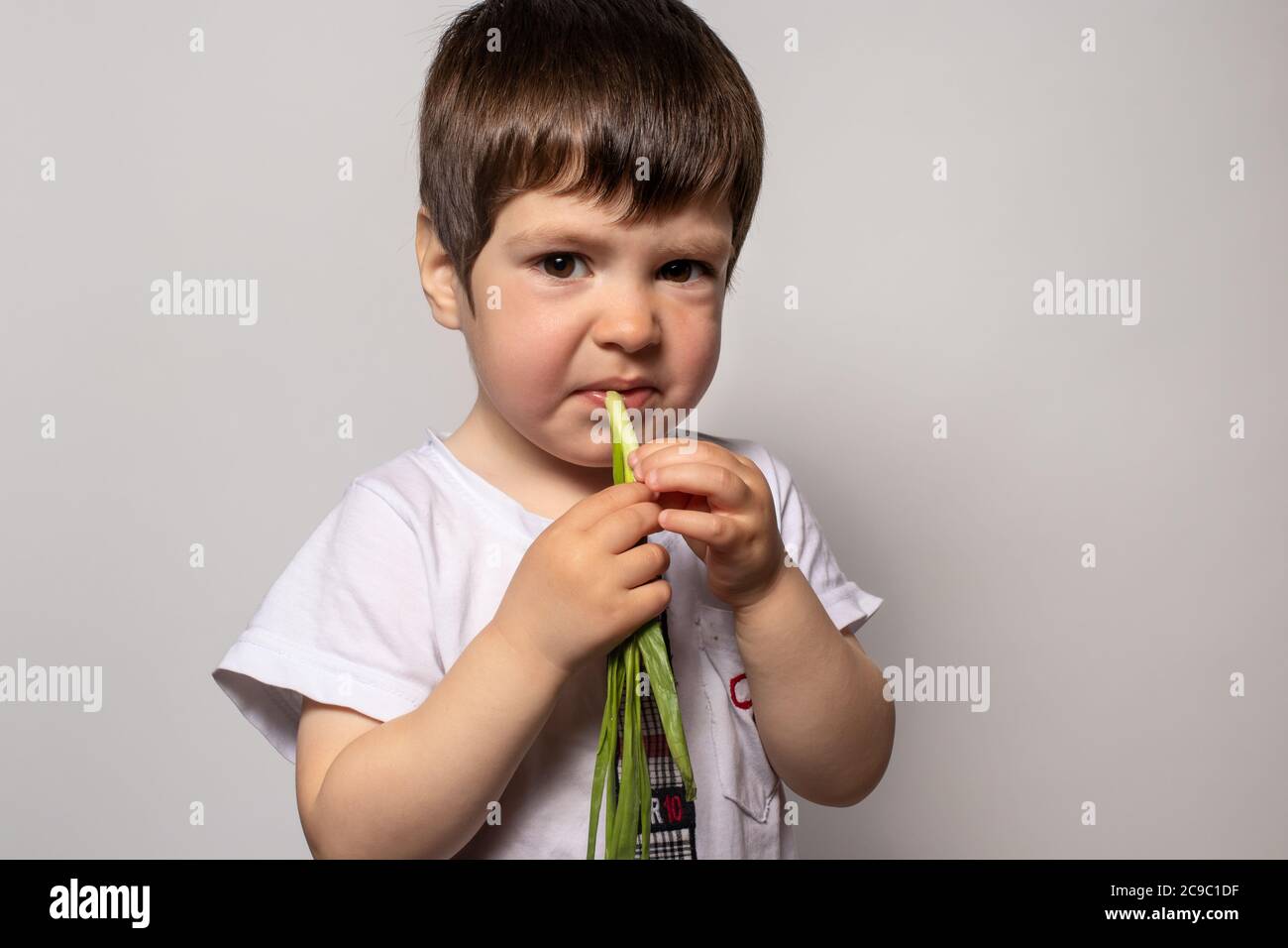 Child boy eats fresh green onions and frowns, twists from his taste