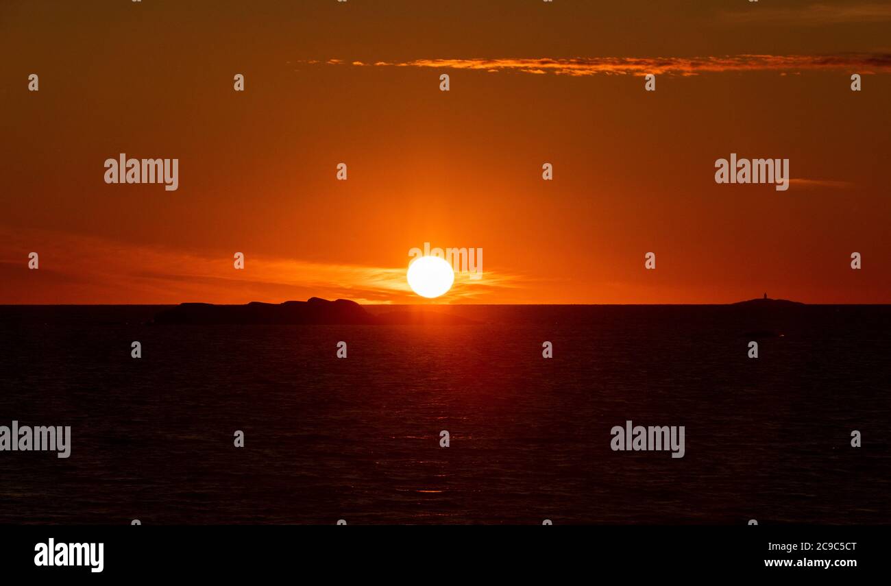 The sun setting in the ocean with small islands and a lighthouse in the horizon. Stock Photo