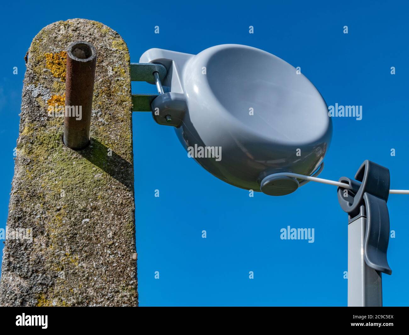 Retractable washing line reel with branding removed attached to a concrete post with blue sky. A washing pole is hanging on the line ready for use Stock Photo Alamy