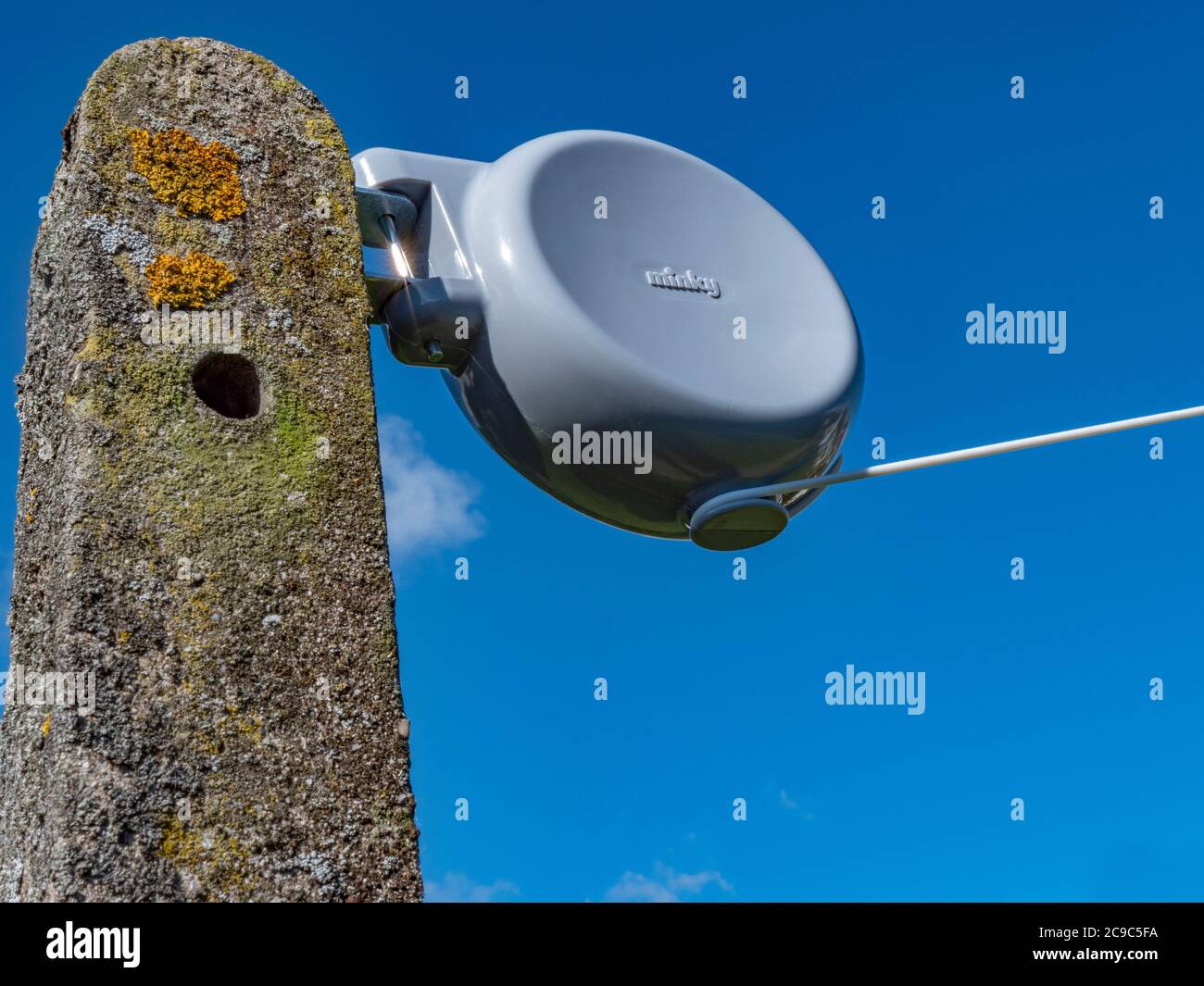 Minky branded retractable washing line reel, attached to a concrete post, with the line tightly pulled out and secured around the reel base. Stock Photo