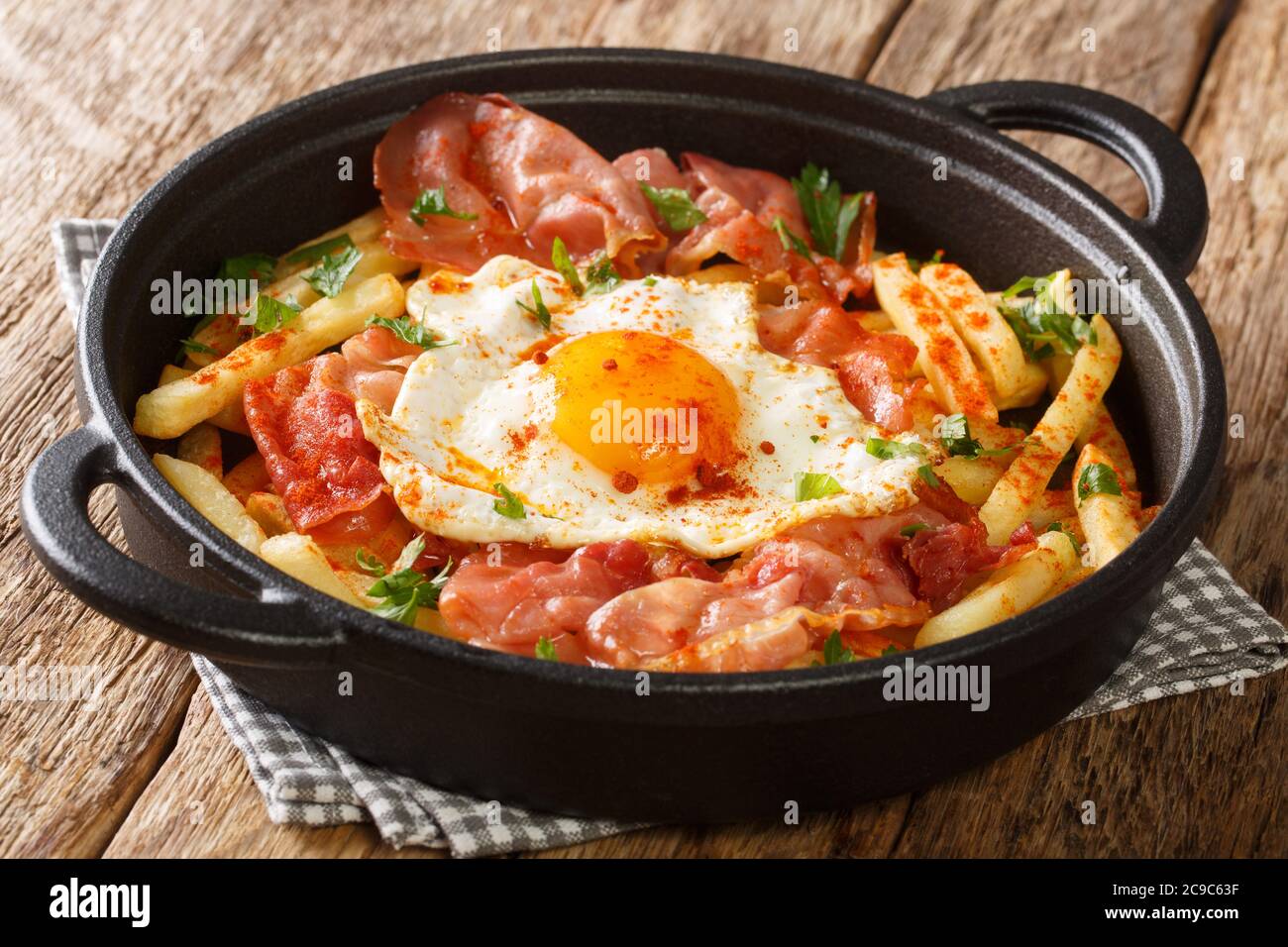 Spanish style fried egg with French fries and jamon close-up in a plate on the table. horizontal Stock Photo