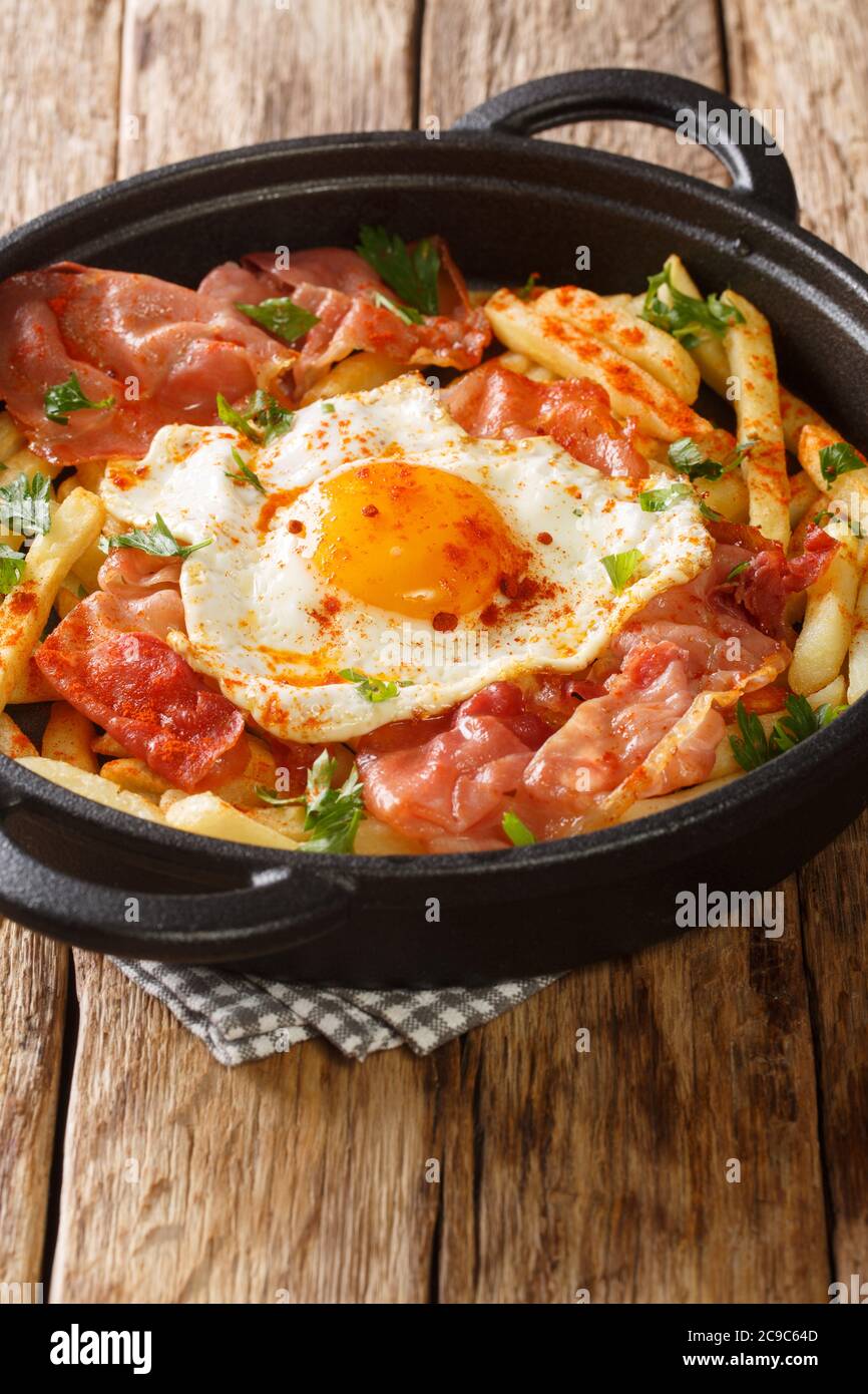 Spanish cuisine fried egg with fries and ham close-up in a plate on the table. vertical Stock Photo