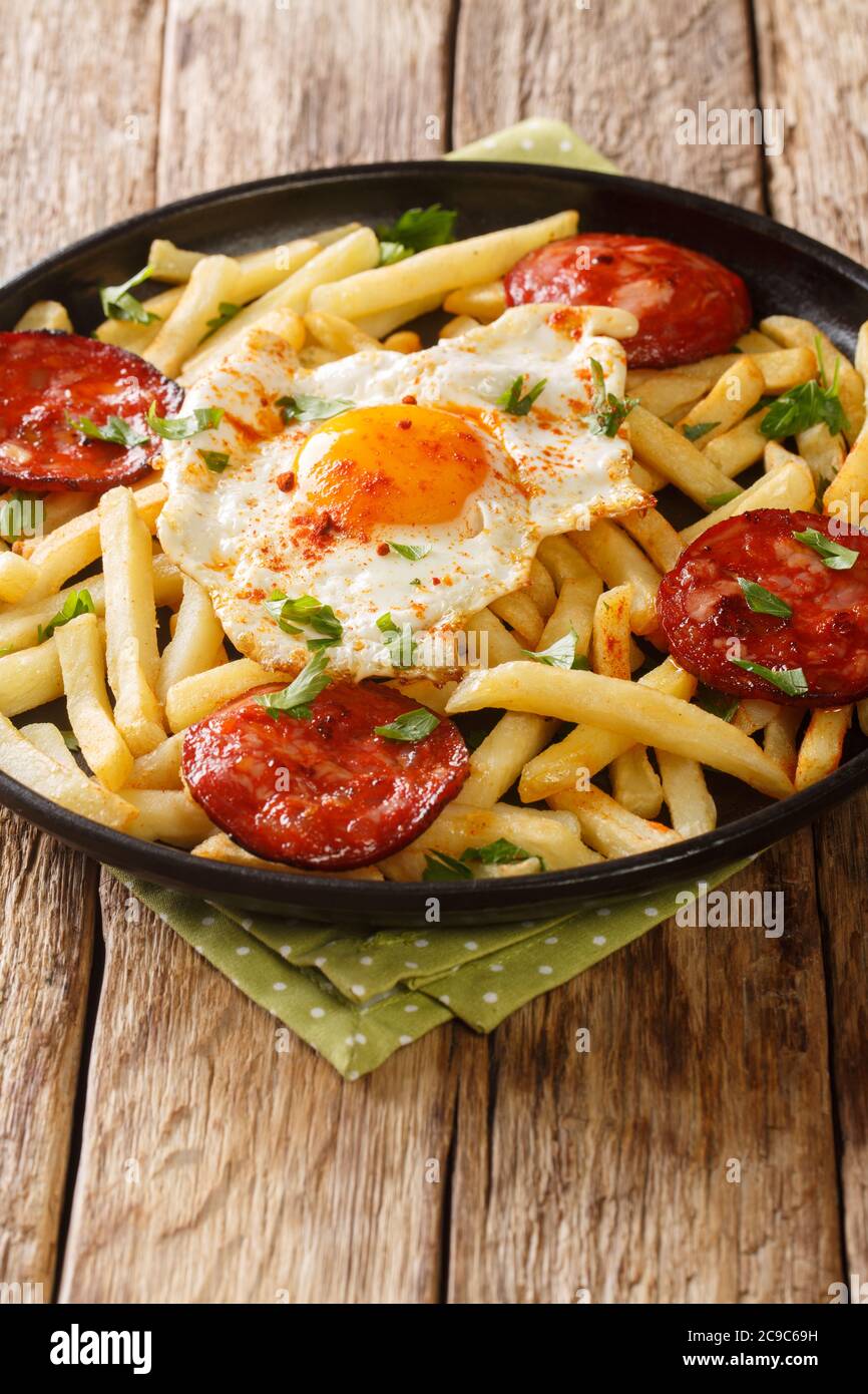Spanish cuisine fried egg with fries and chorizo sausage close-up in a plate on the table. vertical Stock Photo
