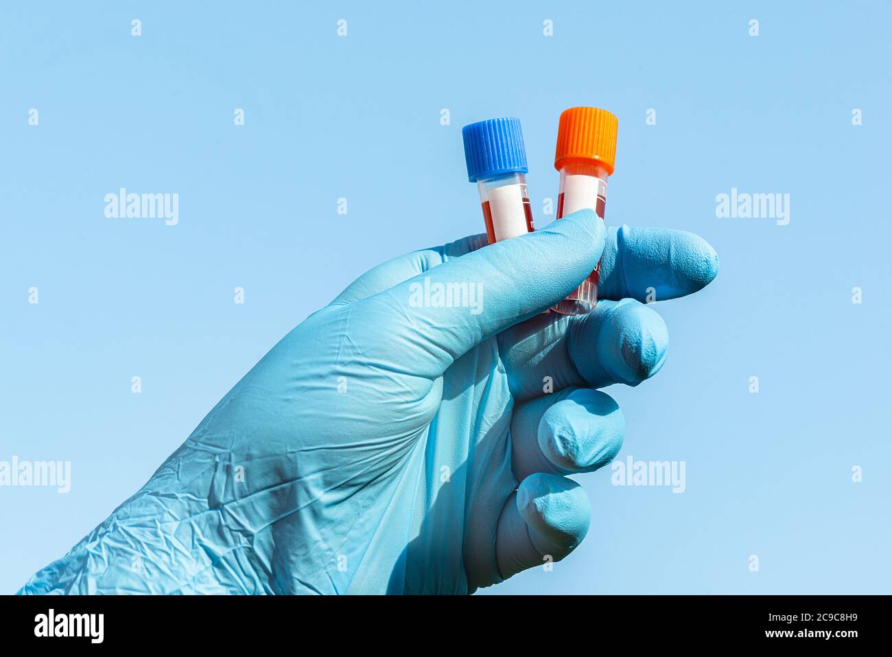 Hands with blue gloves holding two test tubes full of blood blue sky Stock Photo