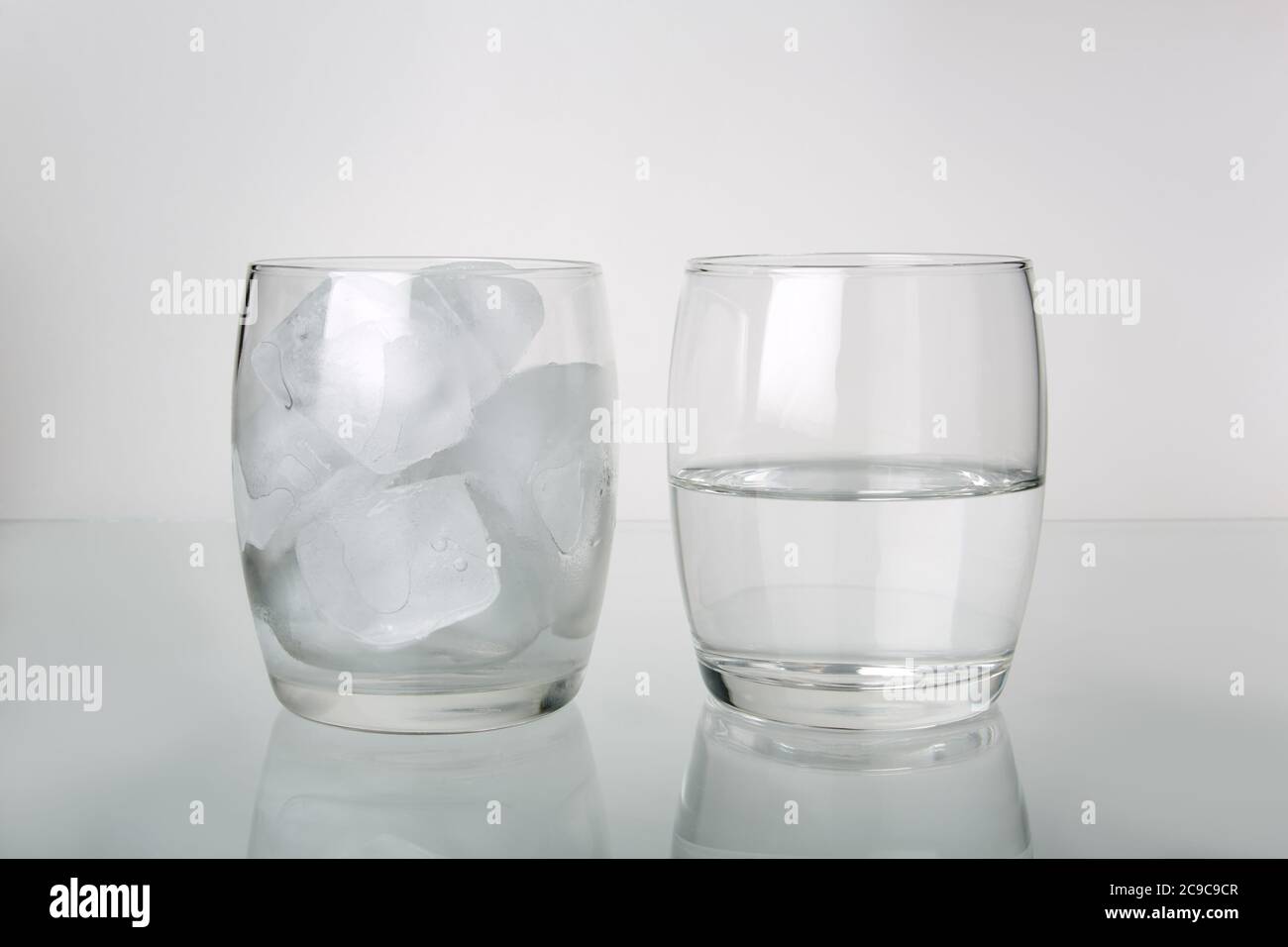 Photograph of two glasses. One glass full of ice with a second glass half full of water to show ice melted. Photographed on a light background. Stock Photo