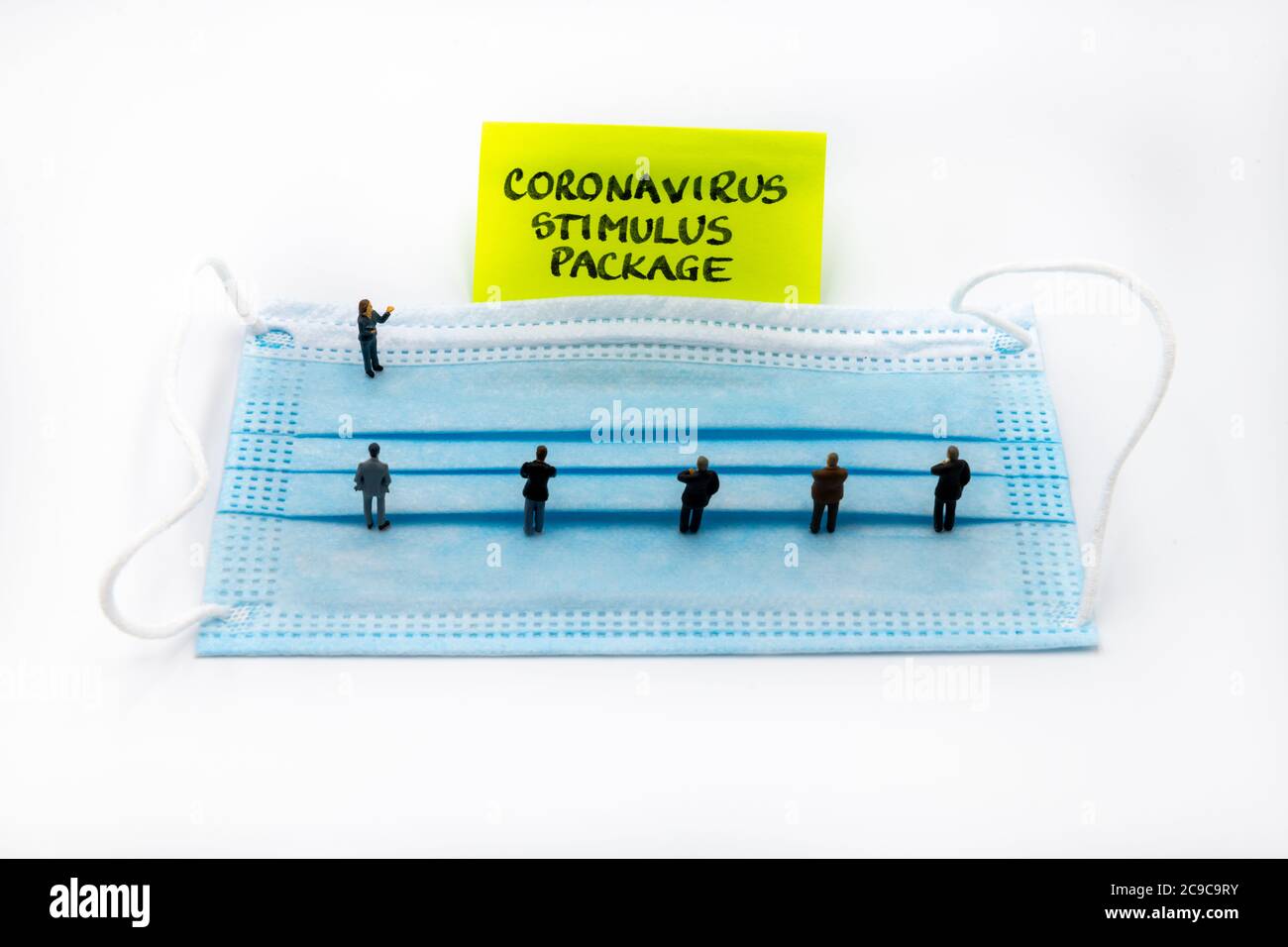 Miniature figurines posed as business people standing socially distanced on medical face mask in a meeting looking at post-it note with Coronavirus Stock Photo