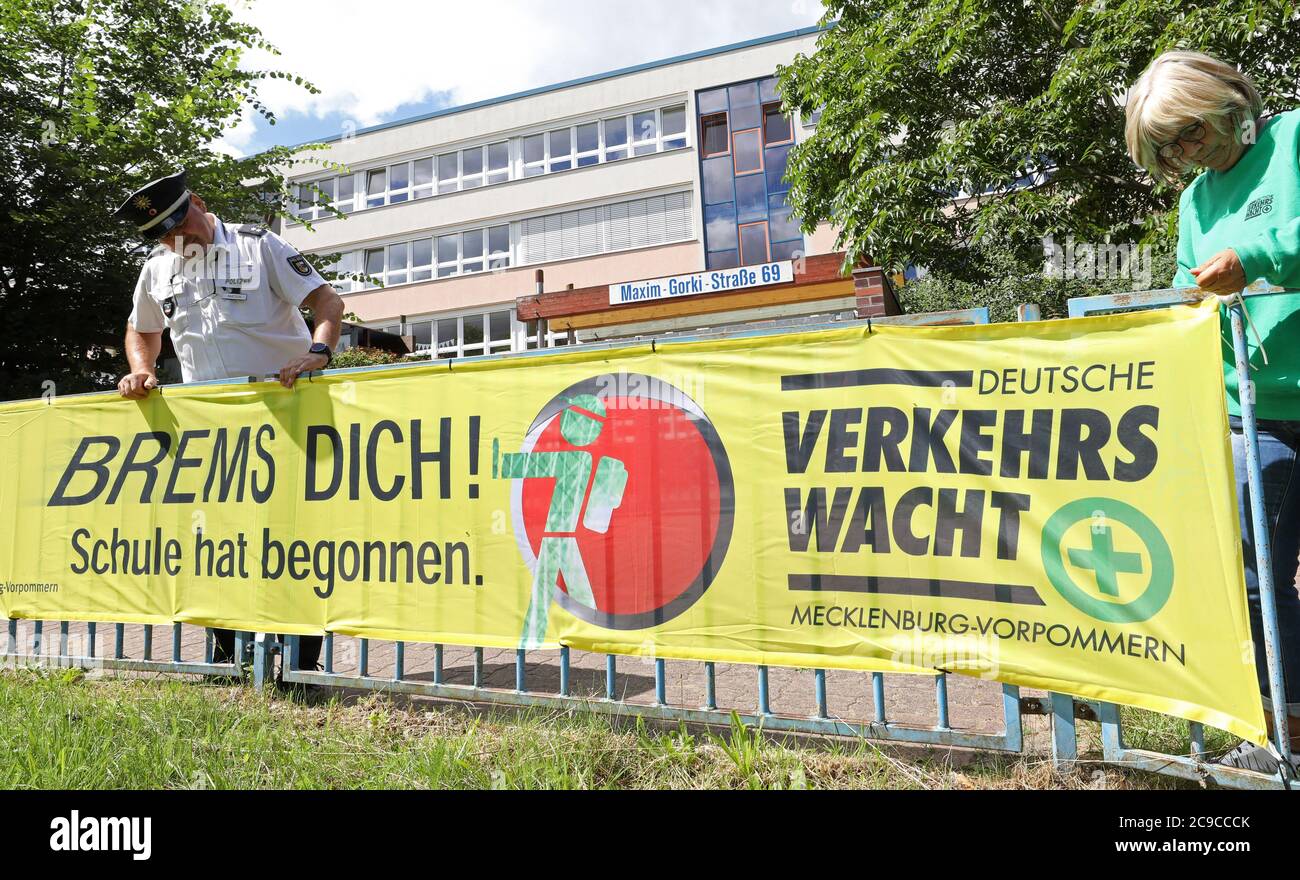 Rostock, Germany. 30th July, 2020. Matthias Bartsch, prevention officer of the Rostock police, and Angelika Stiemer, traffic guard, fasten a banner in front of the primary school at the mill pond with the inscription 'Brems dich! School has begun.'. On 03.08.2020 lessons will begin again for about 150,000 pupils in Mecklenburg-Western Pomerania. Credit: Bernd Wüstneck/dpa-Zentralbild/ZB/dpa/Alamy Live News Stock Photo