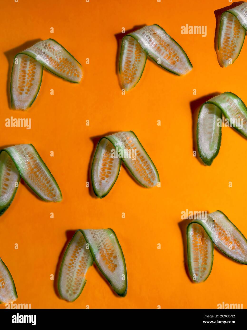 Long cucumber slices arranged on orange background Stock Photo