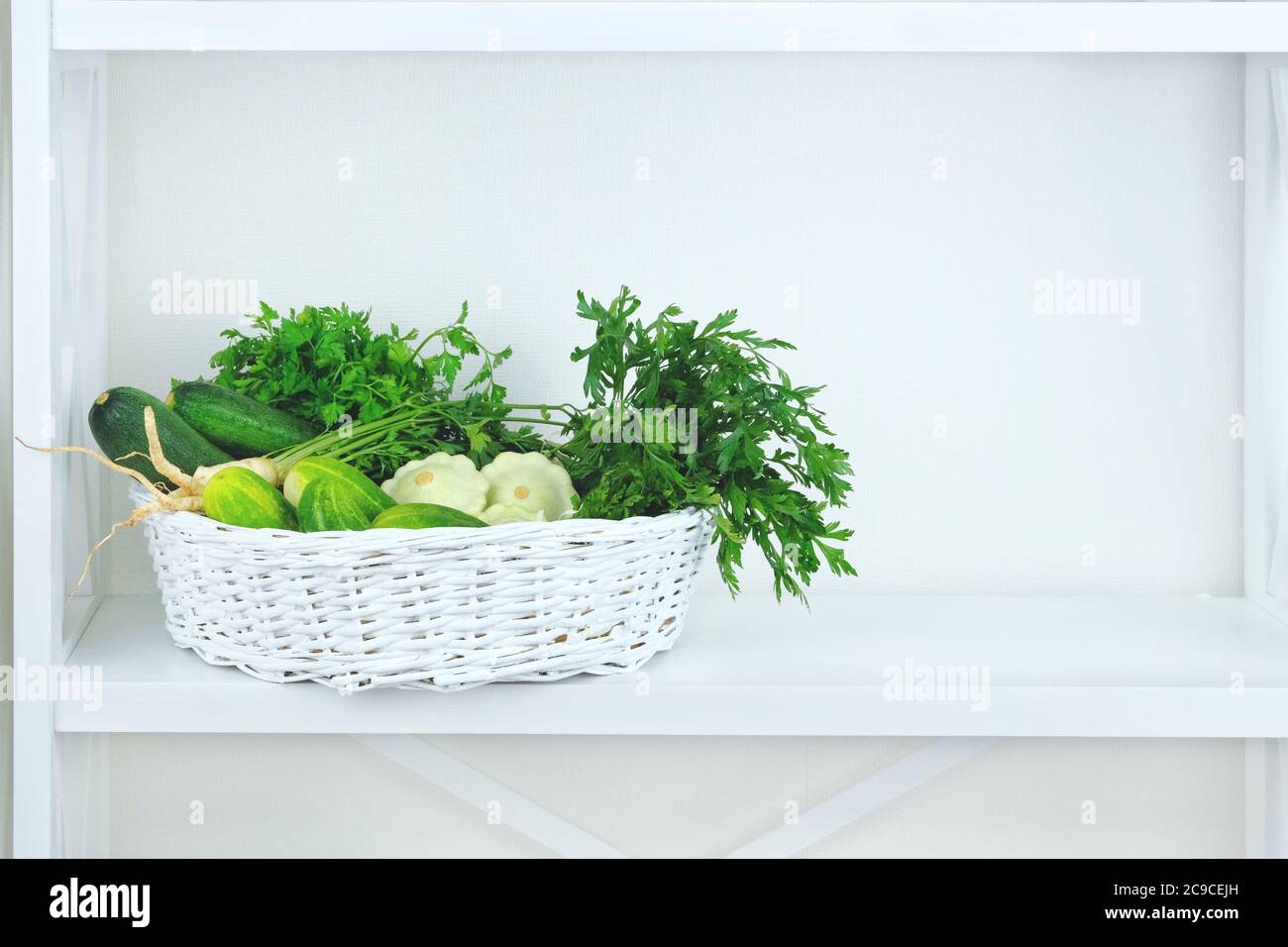 Green autumn vegetables in basket on shelf in wooden rack near a white wall. Copy space for putting text. Stock Photo