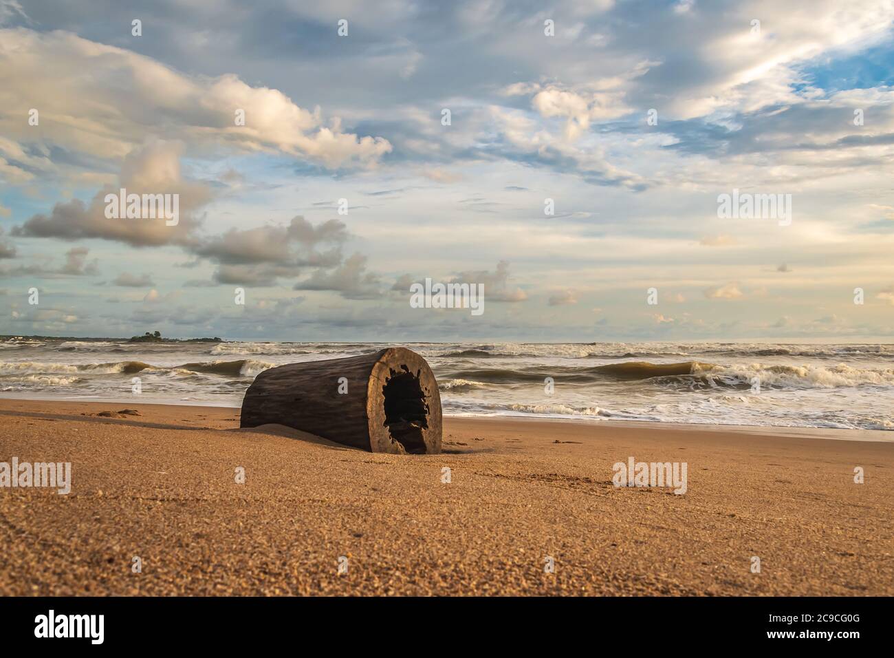Africa's gold coast with a hollow log on the beach during sunset in Axim Ghana West Africa Stock Photo