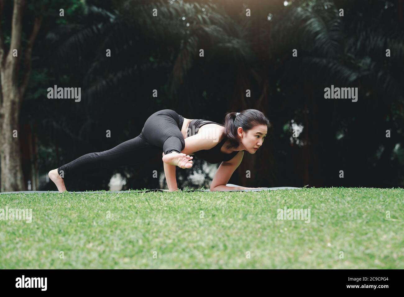Asian woman practicing yoga on mat in outdoor park Stock Photo - Alamy