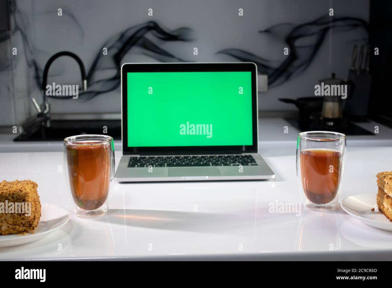 two cups of tea and two pieces of cake in gray kitchen next to laptop ...