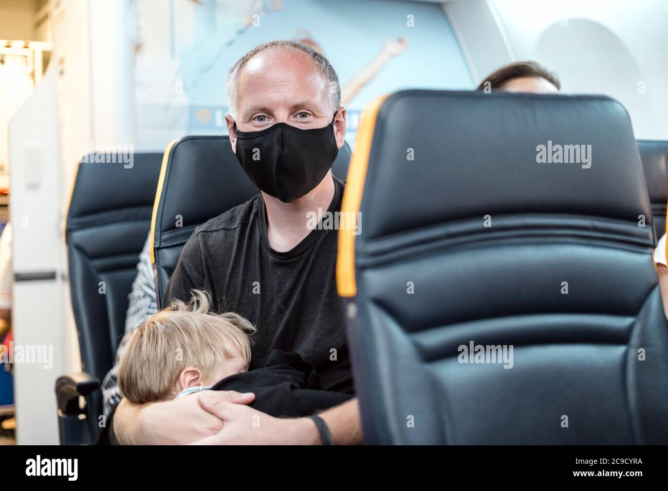 Man in the mask holding his small sleeping son in the airplane Stock Photo