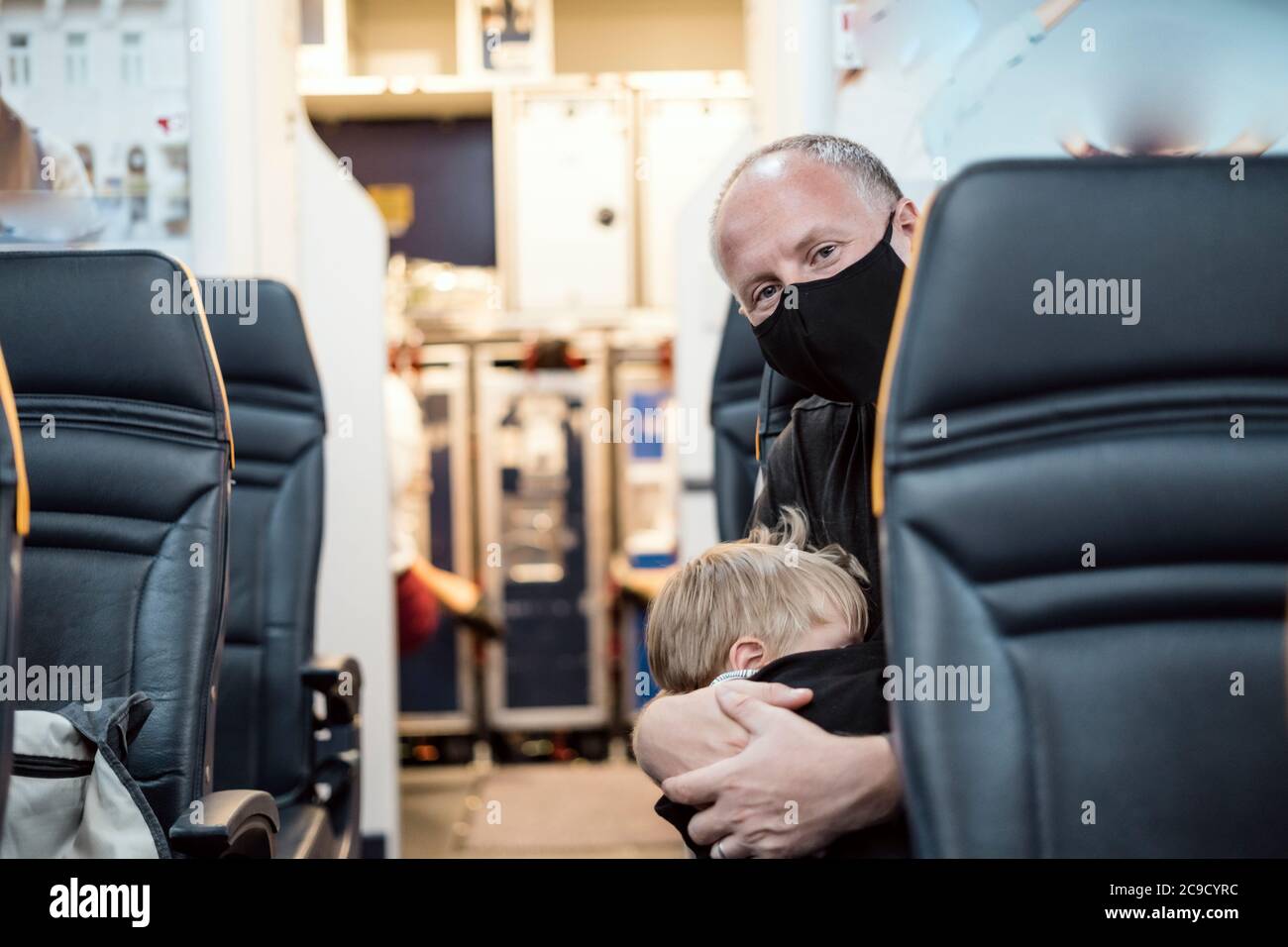 Man in the mask holding his small sleeping son in the airplane Stock Photo