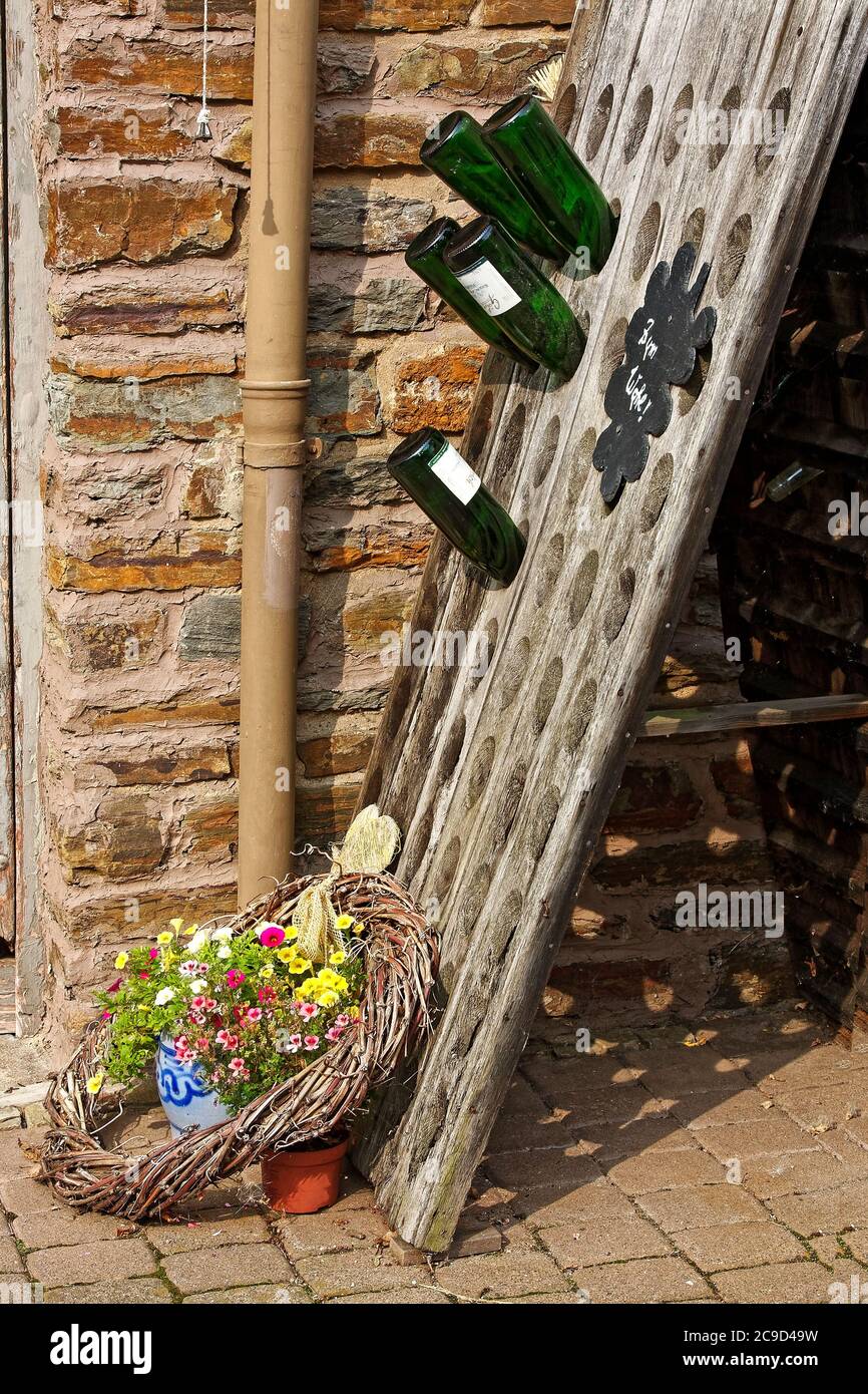 slanted wood rack, holding wine bottles, grapevine wreath, potted flowers, brick wall, cobblestone sidewalk, outdoor decorations, Europe, Zell; German Stock Photo