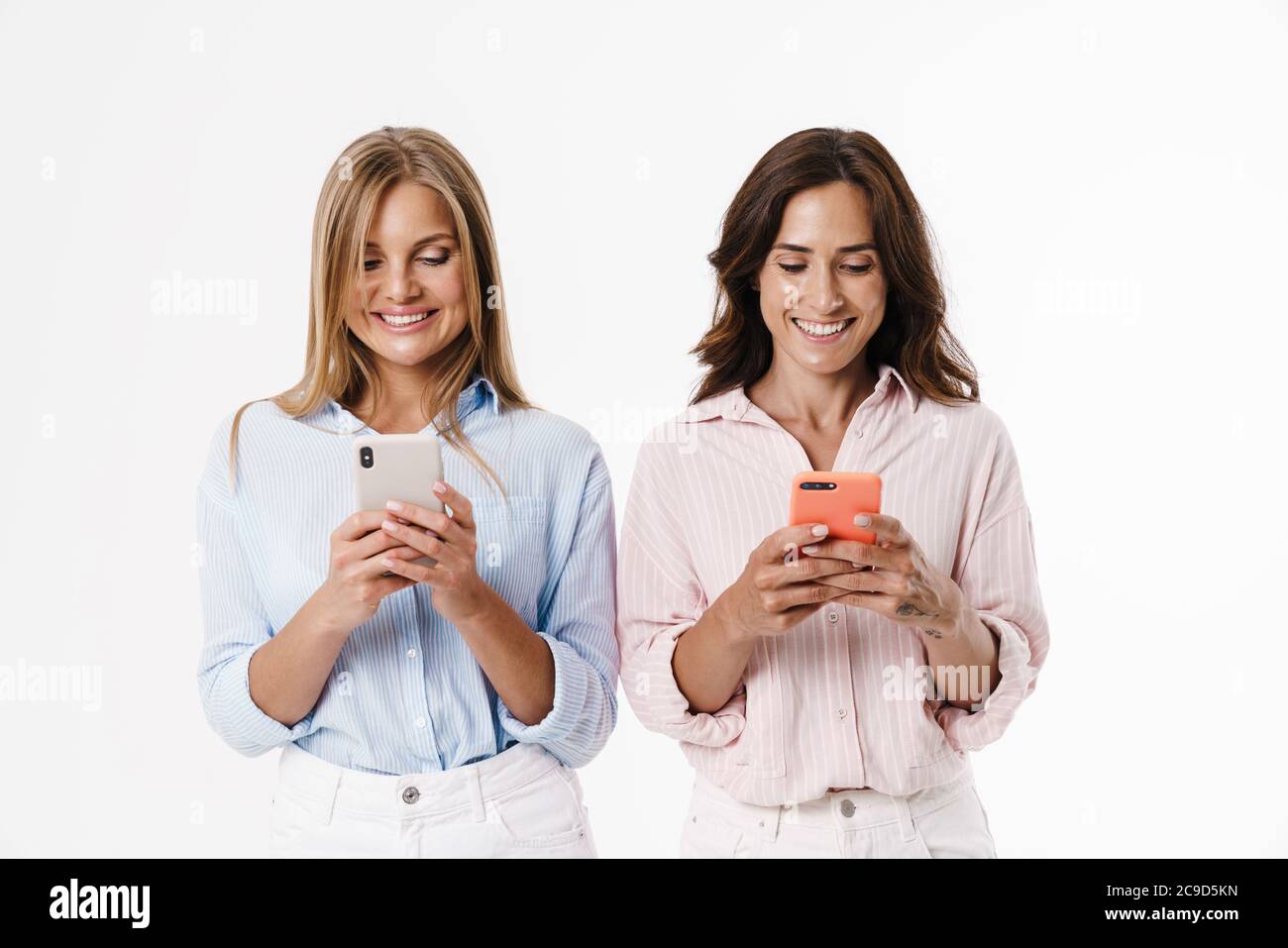 Image of happy charming two women smiling and using mobile phones ...