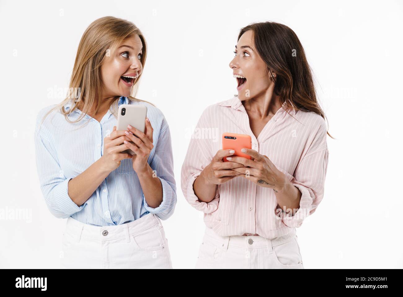 Image of excited two women expressing surprise while using mobile ...