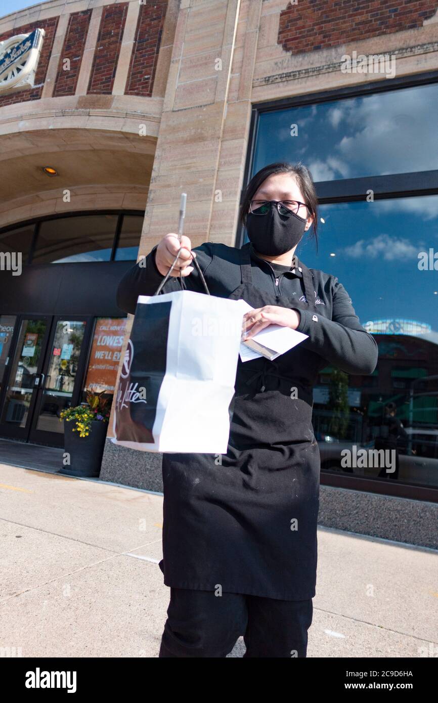 Masked Asian waitperson delivering food from Cafe Latte with curbside service while observing social distancing. St Paul Minnesota MN USA Stock Photo