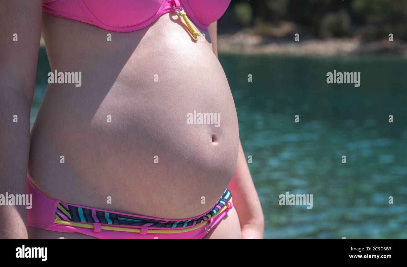 Close up of pregnant womans belly at the sea. Pregnant woman in pink bikini on the beach. Stock Photo