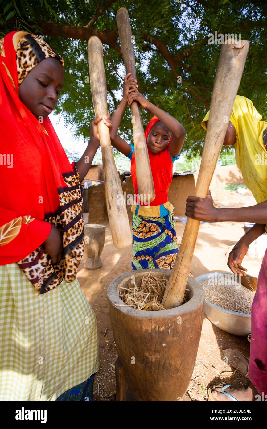 Girls work together to thresh cowpea shells by pounding them with a  mortar and pestle in Tahoua Region, Niger, West Africa. Stock Photo