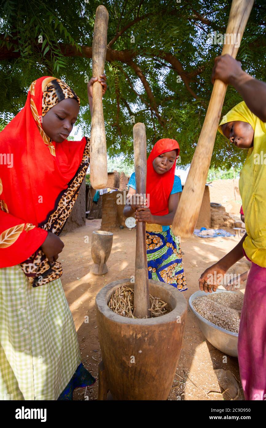 Girls work together to thresh cowpea shells by pounding them with a  mortar and pestle in Tahoua Region, Niger, West Africa. Stock Photo