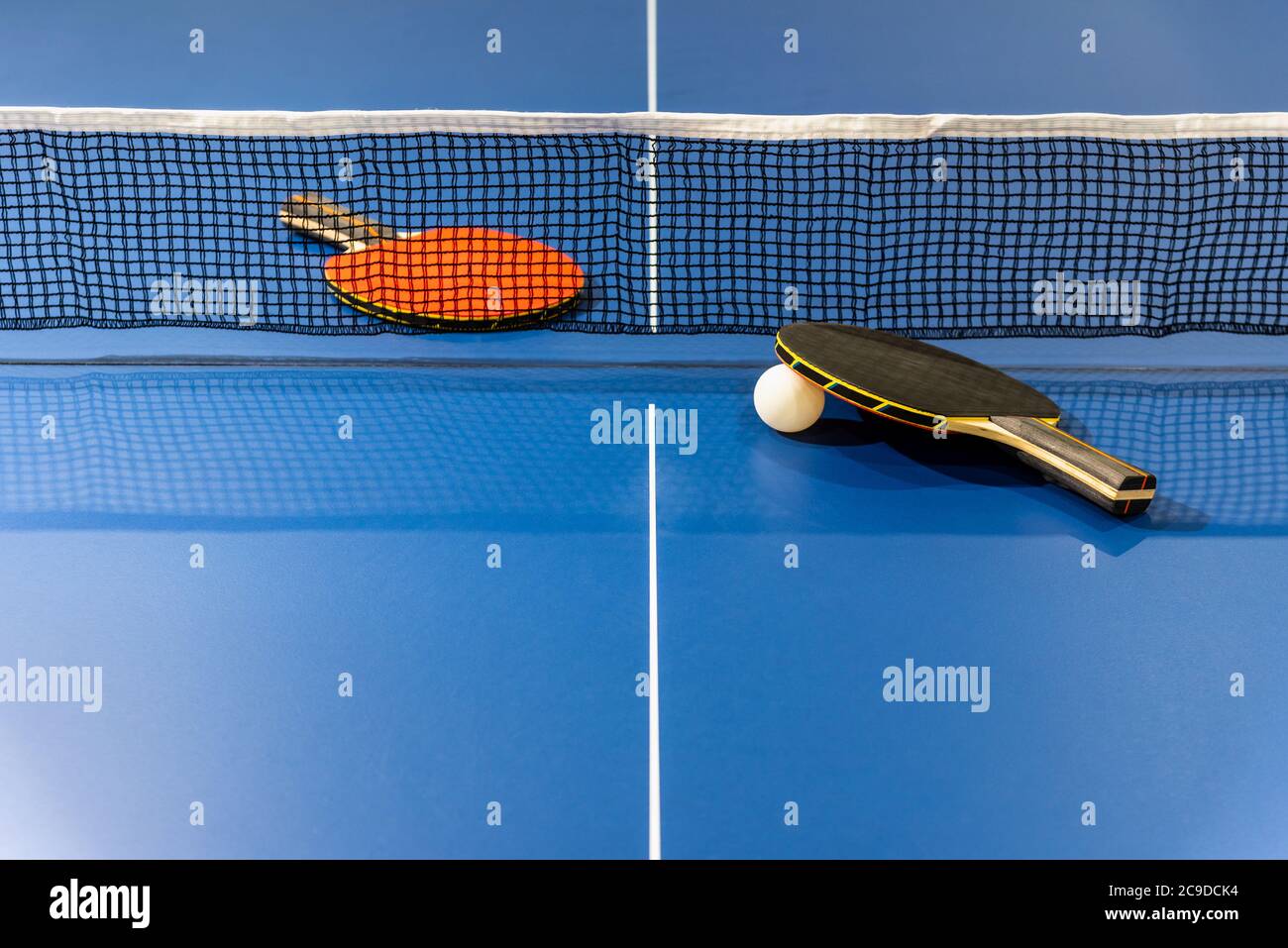 Black and red table tennis racket and a white ball on the blue ping pong table with a net, Two table tennis paddle is a sports competition equipment i Stock Photo