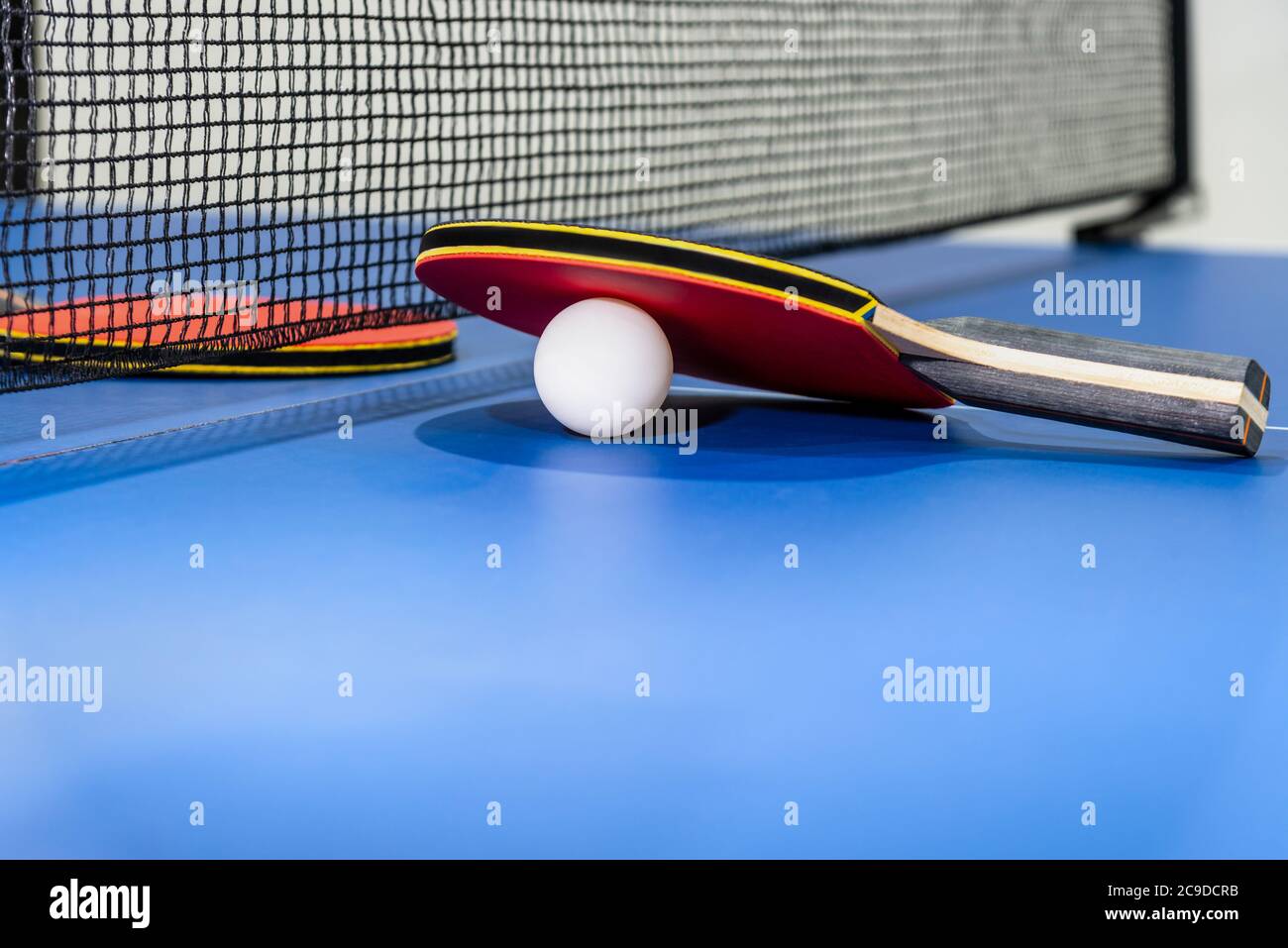 Red table tennis racket and a white ball on the blue ping pong table with a black net, Two table tennis paddle is a sports competition equipment indoo Stock Photo