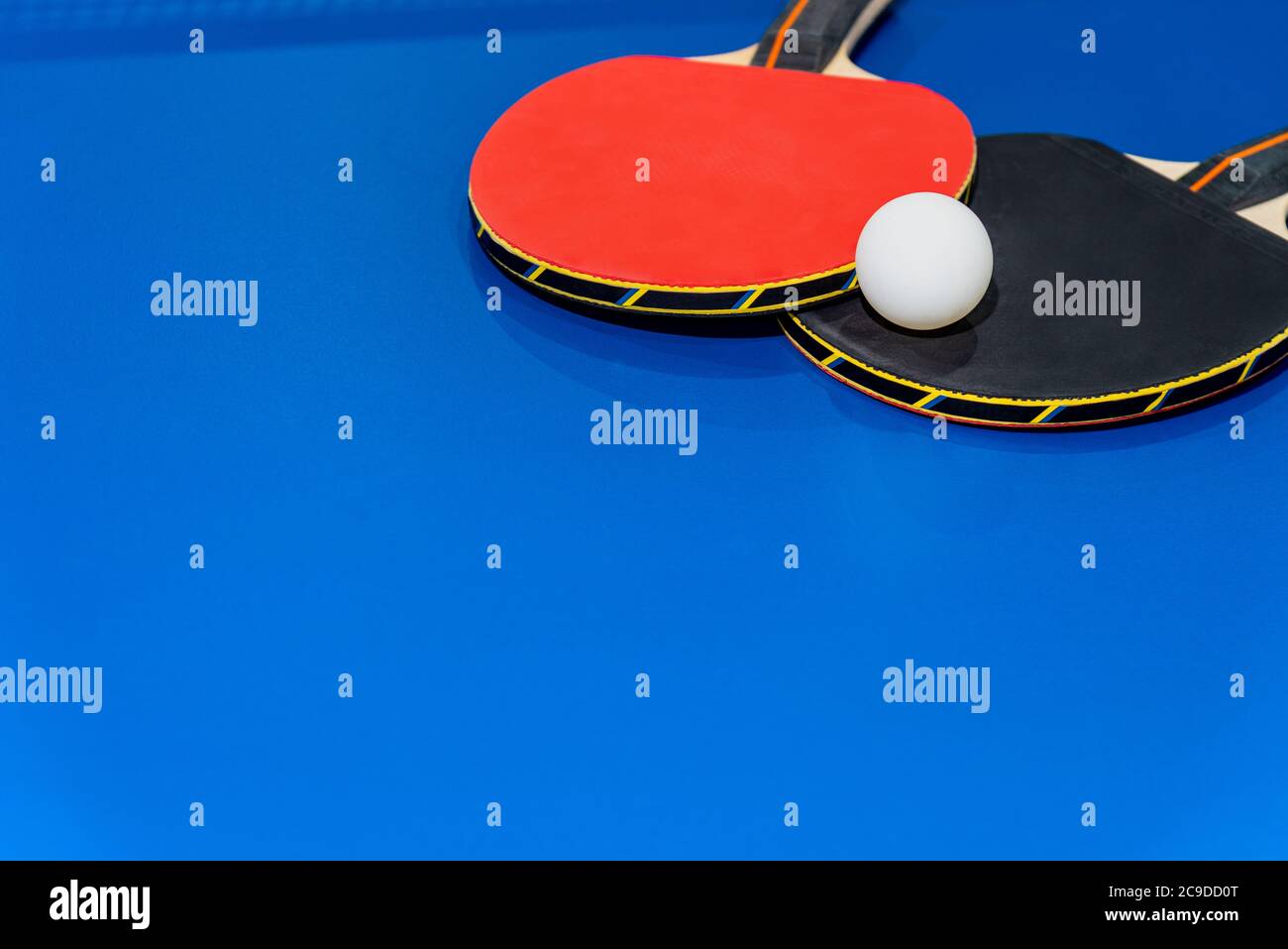 Black and red table tennis racket and a white ping pong ball on the blue ping pong table, Two table tennis paddle is a sports competition equipment fo Stock Photo