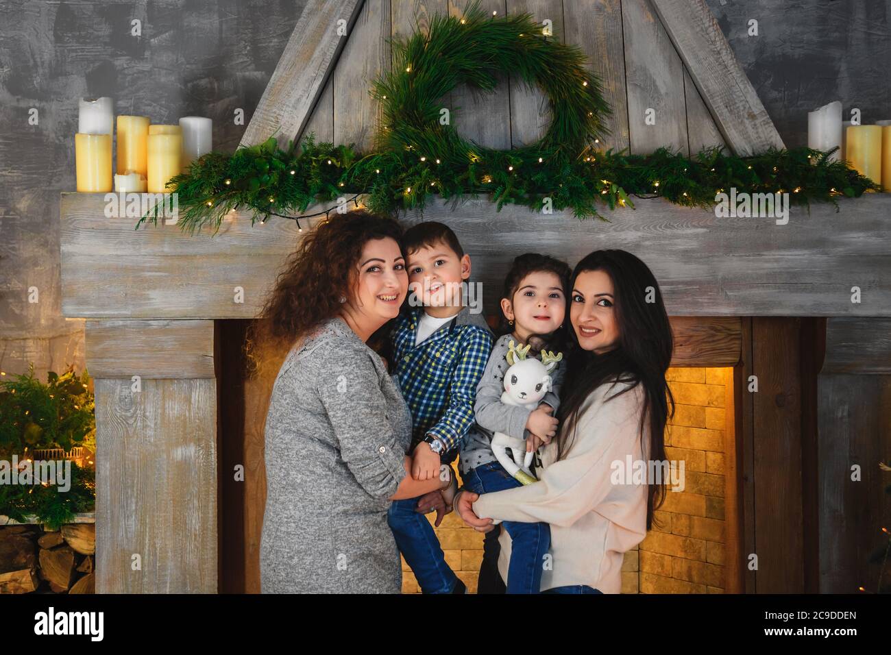 Christmas family portrait of happy smiling mothers hugging their children near to fireplace decorated with fir and garland at home. Winter holiday Stock Photo