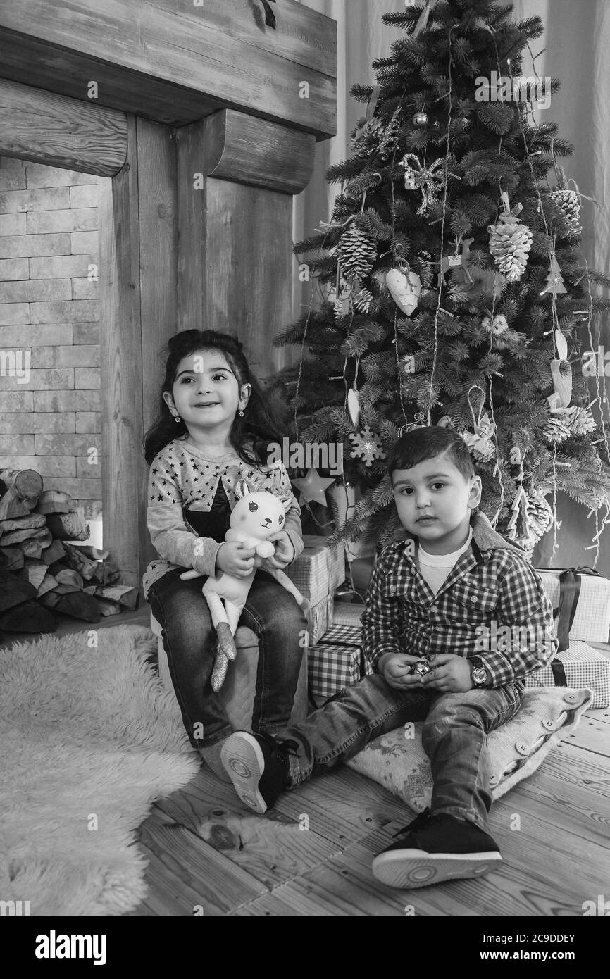 Christmas portrait of beautiful smiling little kids sitting on floor with presents under the christmas tree. Winter holiday Xmas and New Year concept Stock Photo