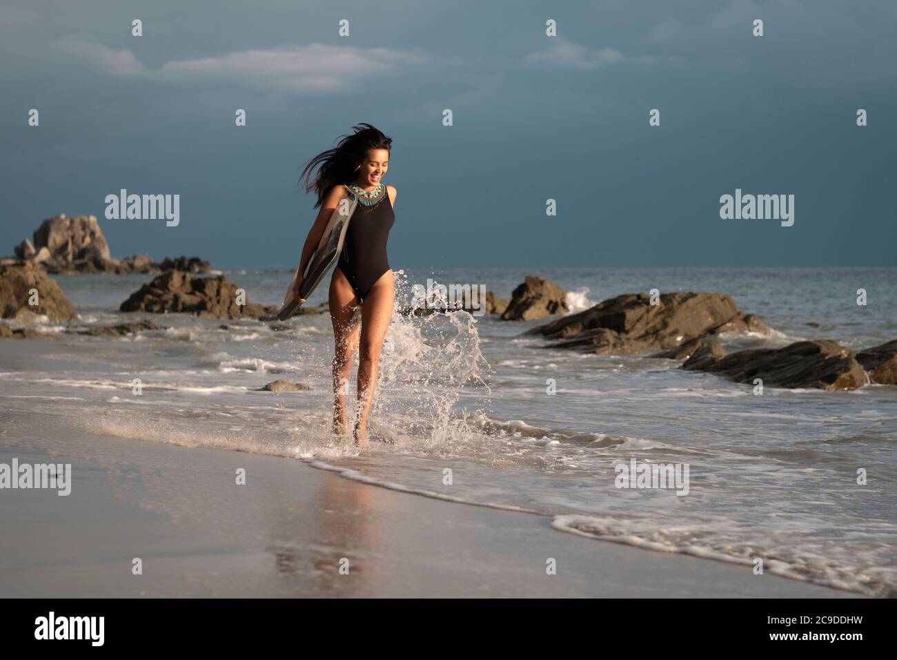 Young woman with boogie board running at a rocky beach on Mexico's Pacific coast Stock Photo