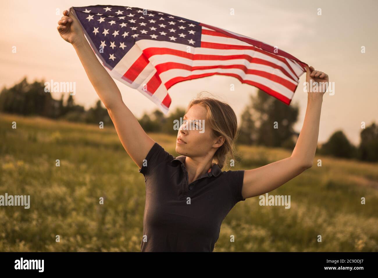 Girl with American flag runs in nature at sunset. Independence Day USA. Patriot Day Stock Photo
