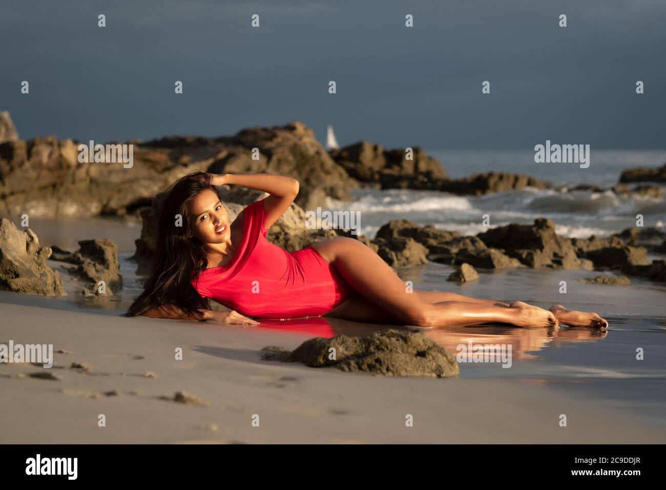 Young latina woman in red swimsuit posing at sunset hours at a beach Stock Photo