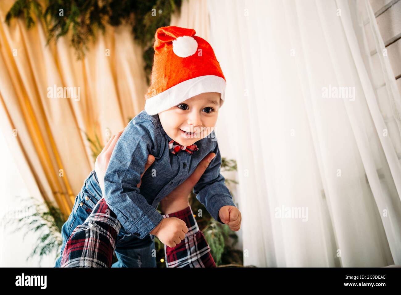 Christmas family portrait of happy smiling little boy in red santa hat in father's hands. Winter holiday Xmas and New Year concept Stock Photo