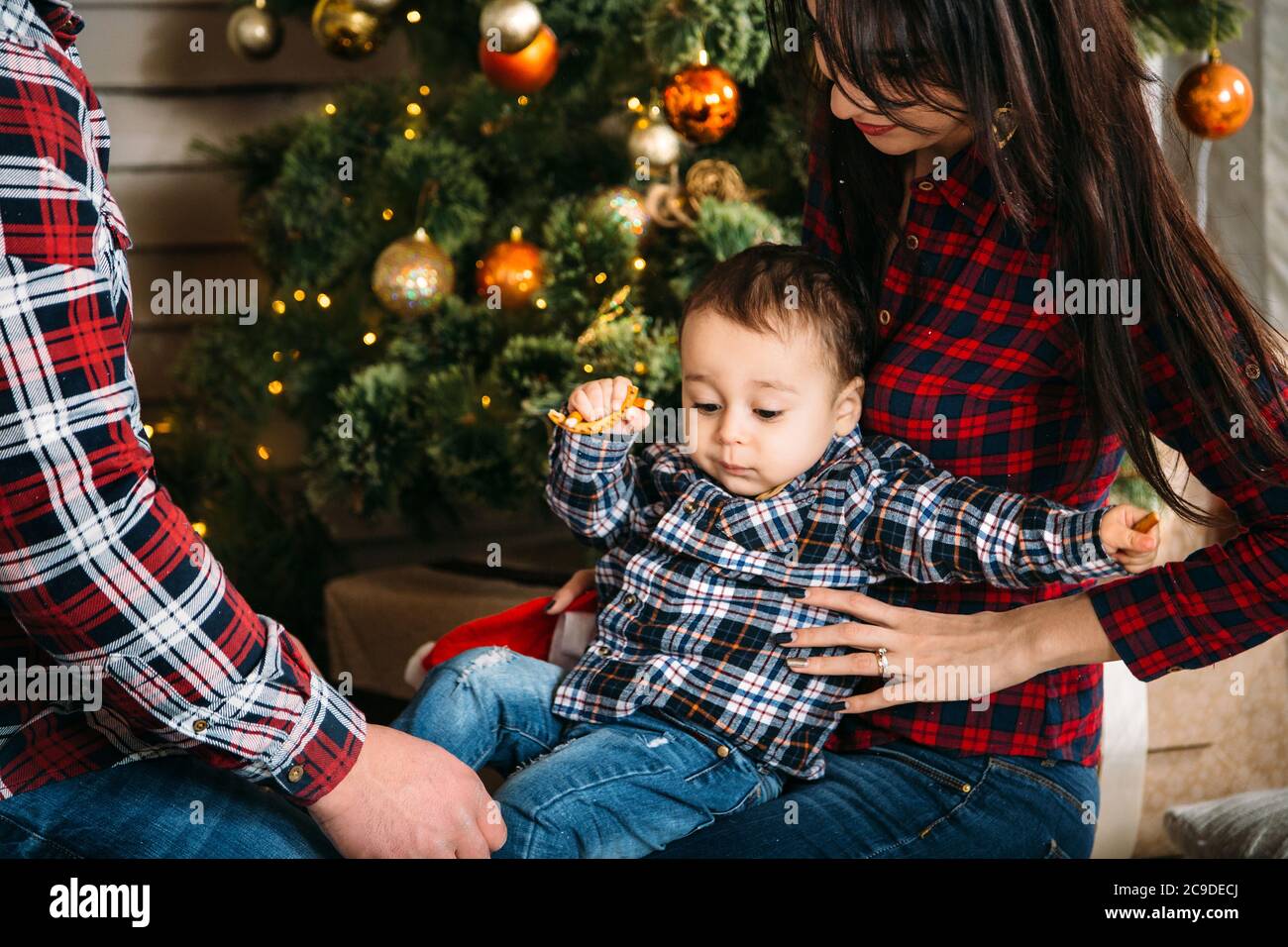 Christmas family portrait of young happy smiling parents playing with small child near the christmas tree. Winter holiday Xmas and New Year concept Stock Photo