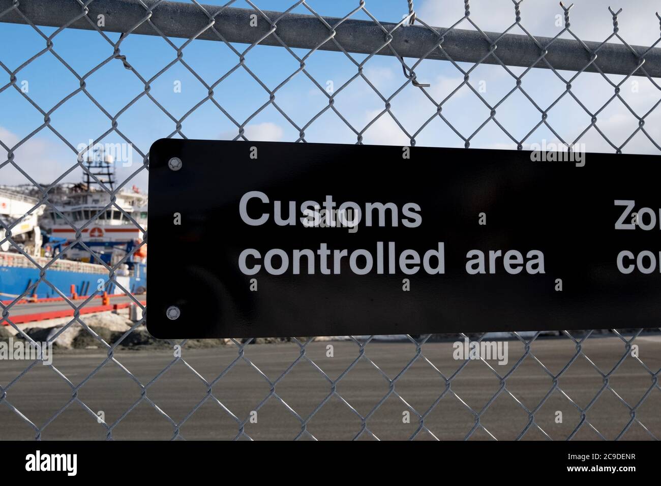 A black and white fence with a sign attached to a chain link industrial boarder. It has customs controlled area in white text. Stock Photo