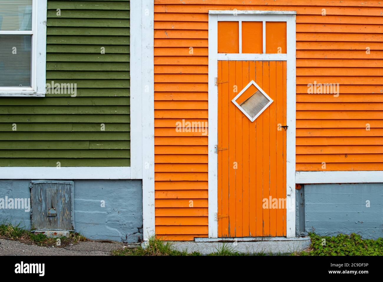 An orange wooden exterior door with a diamond shaped window in a building with orange and green wood clapboard. Stock Photo