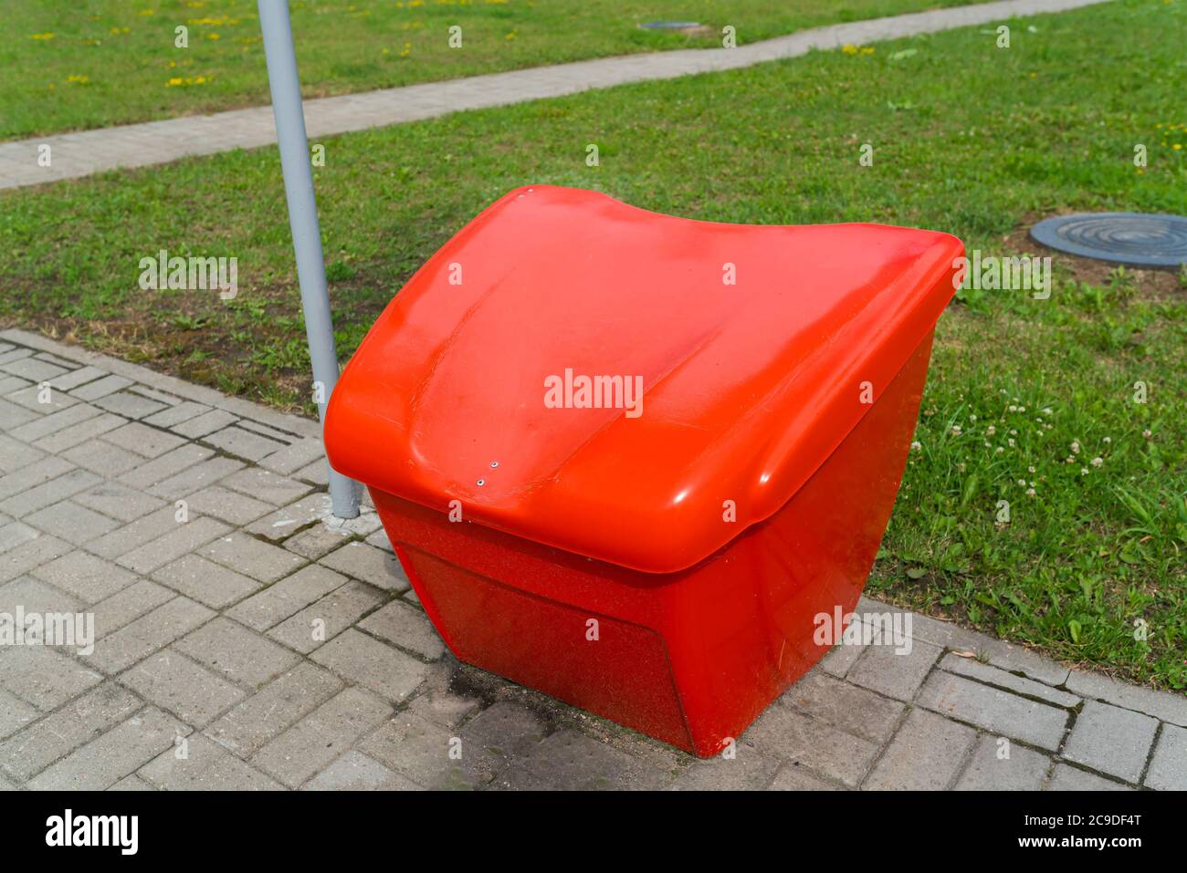Fire-fighting red sand container on the street on a tile on a background of green grass. High quality photo Stock Photo